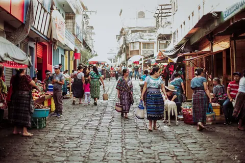 Lively market scene on cobblestone street with vendors and a diverse crowd in traditional attire.
