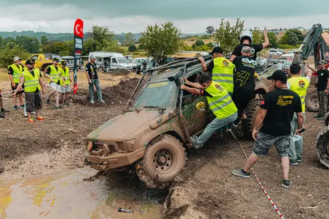 Dynamic offroad racing event with a muddy vehicle and active crew near an event area.
