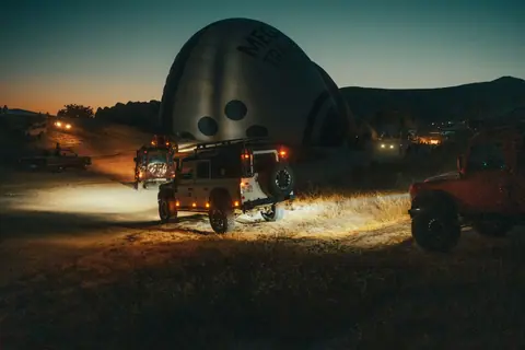 4x4 vehicles prepare for hot air balloon launch at dusk, showcasing adventure spirit.