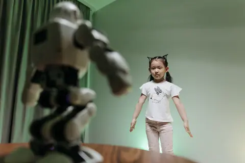 An Asian child interacts with a humanoid robot indoors, embracing innovation and play.