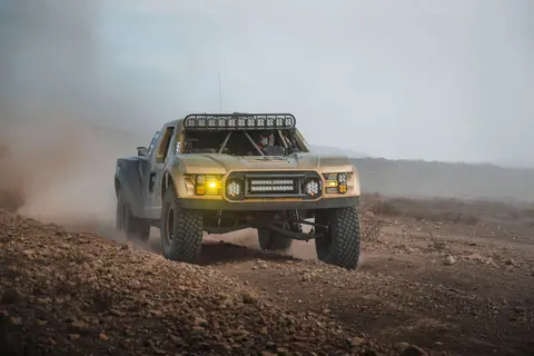 Dynamic shot of a powerful off-road truck racing in the Baja California desert, kicking up dust.