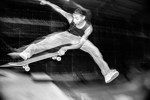 A skateboarder performs an aerial trick indoors in a high-energy black and white photo.