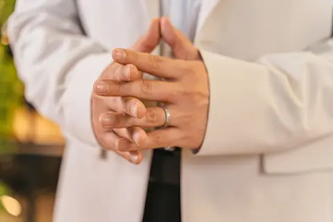 A close-up of hands clasped showing a ring and white suit details.