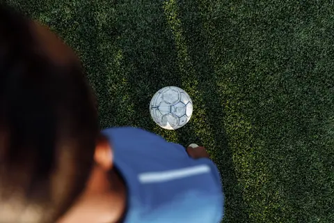 A top-down view of a soccer player preparing to kick a ball on a grass field.