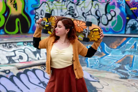 Young woman with skateboard rests by colorful graffiti at an urban skatepark.