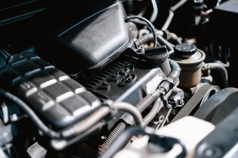 Detailed view of car engine parts, showcasing cables and components with bright lighting.