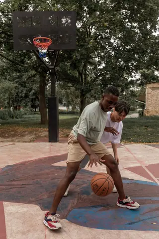 Full body young determined diverse sportsmen in activewear playing basketball together on sports ground on summer day
