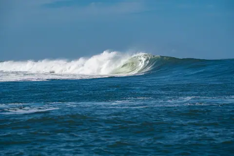 A powerful ocean wave crashes under a clear blue sky, showcasing the beauty of nature.
