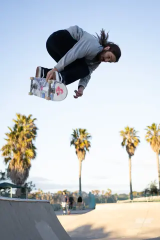 Skilled skateboarder executing a high jump at a skate park with palm trees in the background.