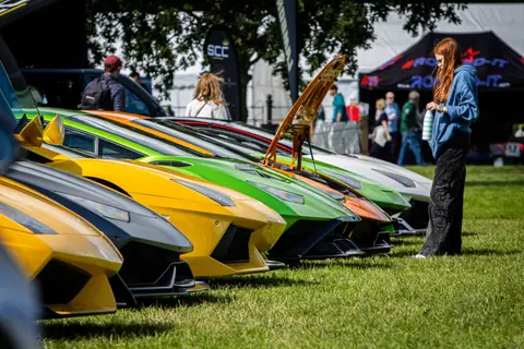 A lineup of colorful Lamborghinis displayed outdoors with onlookers.