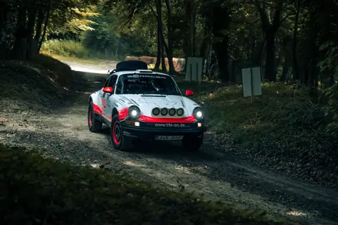 A Porsche rally car speeding through a forest track in England, capturing the thrill of motorsport.