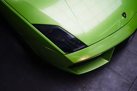 Close-up shot of a vibrant green sports car headlight and hood, showcasing sleek design.