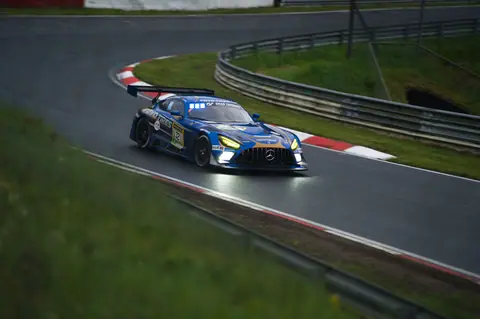A blue sports car speeds through a racetrack corner at Nordschleife, showcasing precision driving.