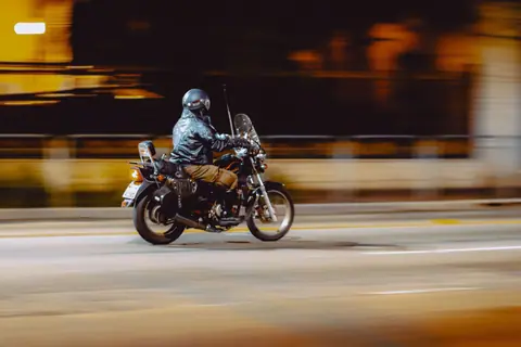 Faceless man in helmet riding motorbike on empty asphalt city road at night