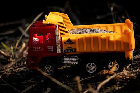 A vibrant toy dump truck filled with gravel, captured outdoors in natural lighting.