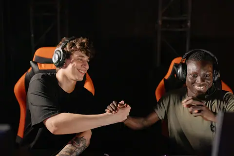 Two young gamers shaking hands and celebrating a win together indoors.