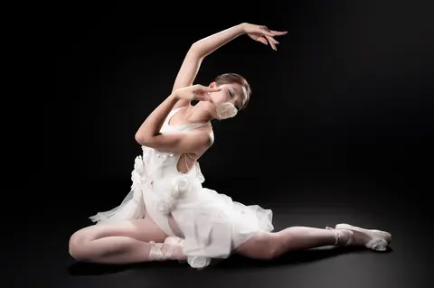 A graceful ballet dancer in a white dress performs on a dark stage, embodying elegance and poise.