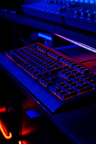 A gaming keyboard illuminated with red and blue LED lights on a dark desktop setup.