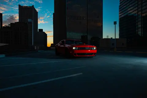 A red sports car parked in a city with skyscrapers and dramatic twilight sky.