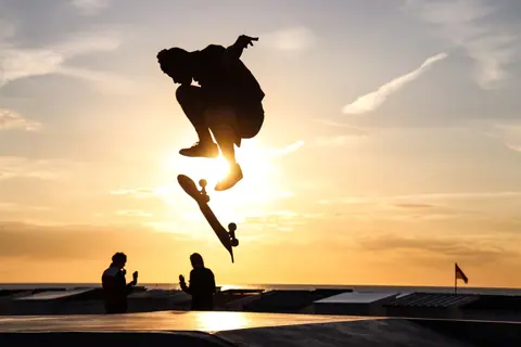 Dramatic silhouette of a skateboarder mid-air against a vibrant sunset sky in Calais, France.