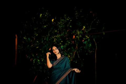 A woman poses in a traditional saree against a dark nighttime backdrop.