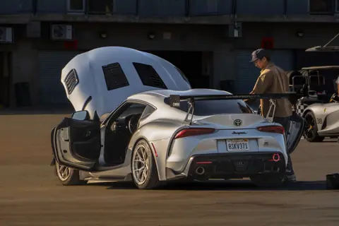 Silver Toyota Supra parked with open doors at a race track in California.