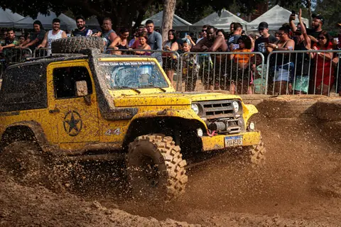 A yellow off-road vehicle splashes through mud in a thrilling racing event, watched by an enthusiastic crowd.