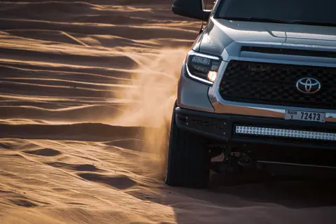 Close-up shot of a Toyota truck navigating desert sand, stirring up dust.