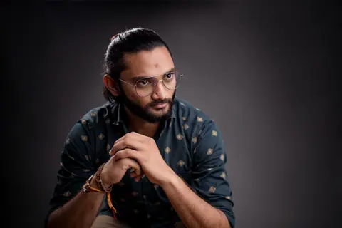 Capture of a man with glasses posing in a studio setting, showcasing modern fashion style.