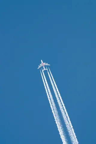 A jet flies high in a clear blue sky leaving distinct contrails behind it.