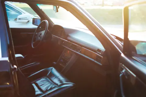A luxurious car interior with an open door, highlighted by warm sunlight casting through the window.